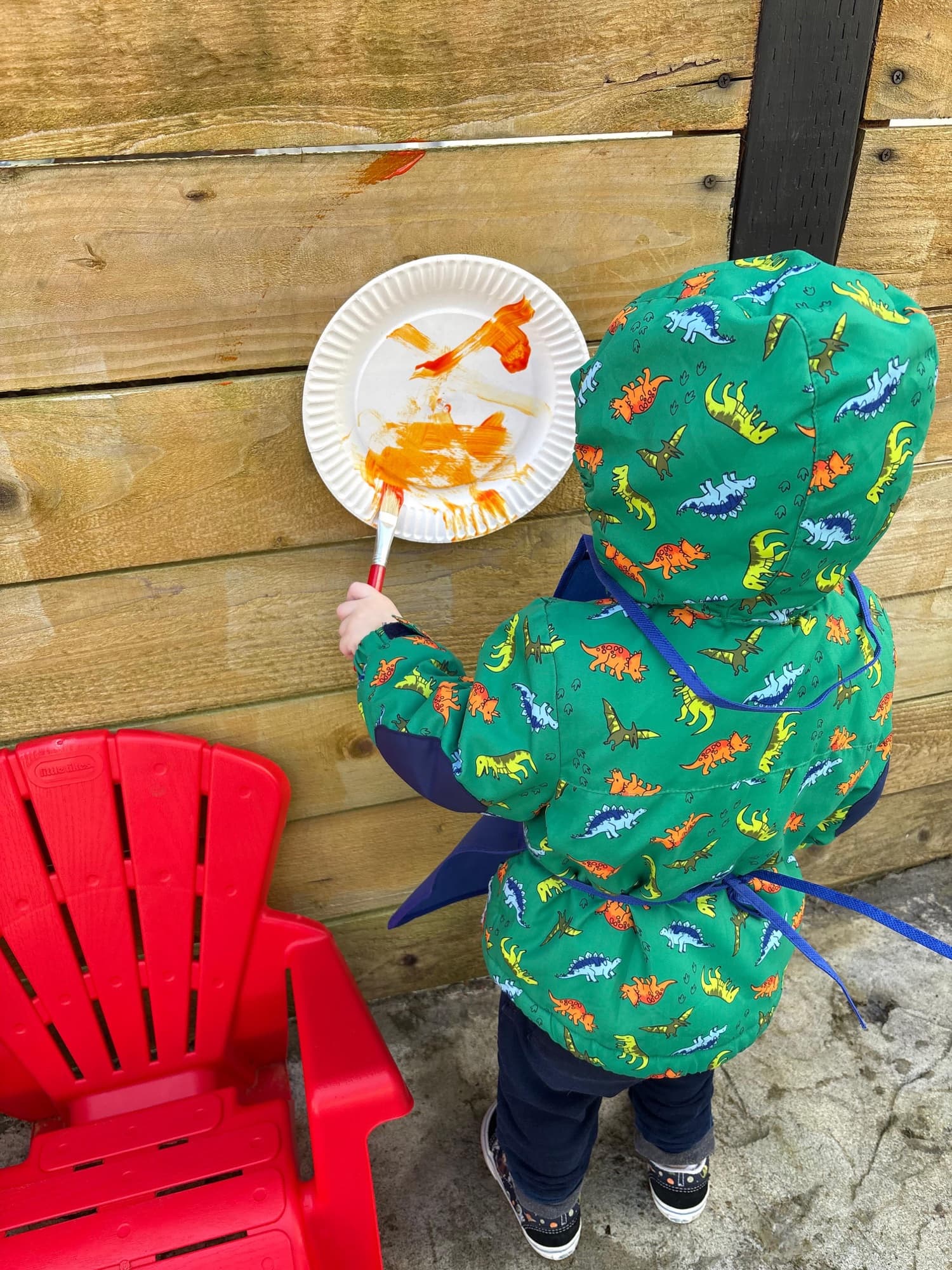 A child in a dinosaur jacket painting outdoors at Rising Stars
