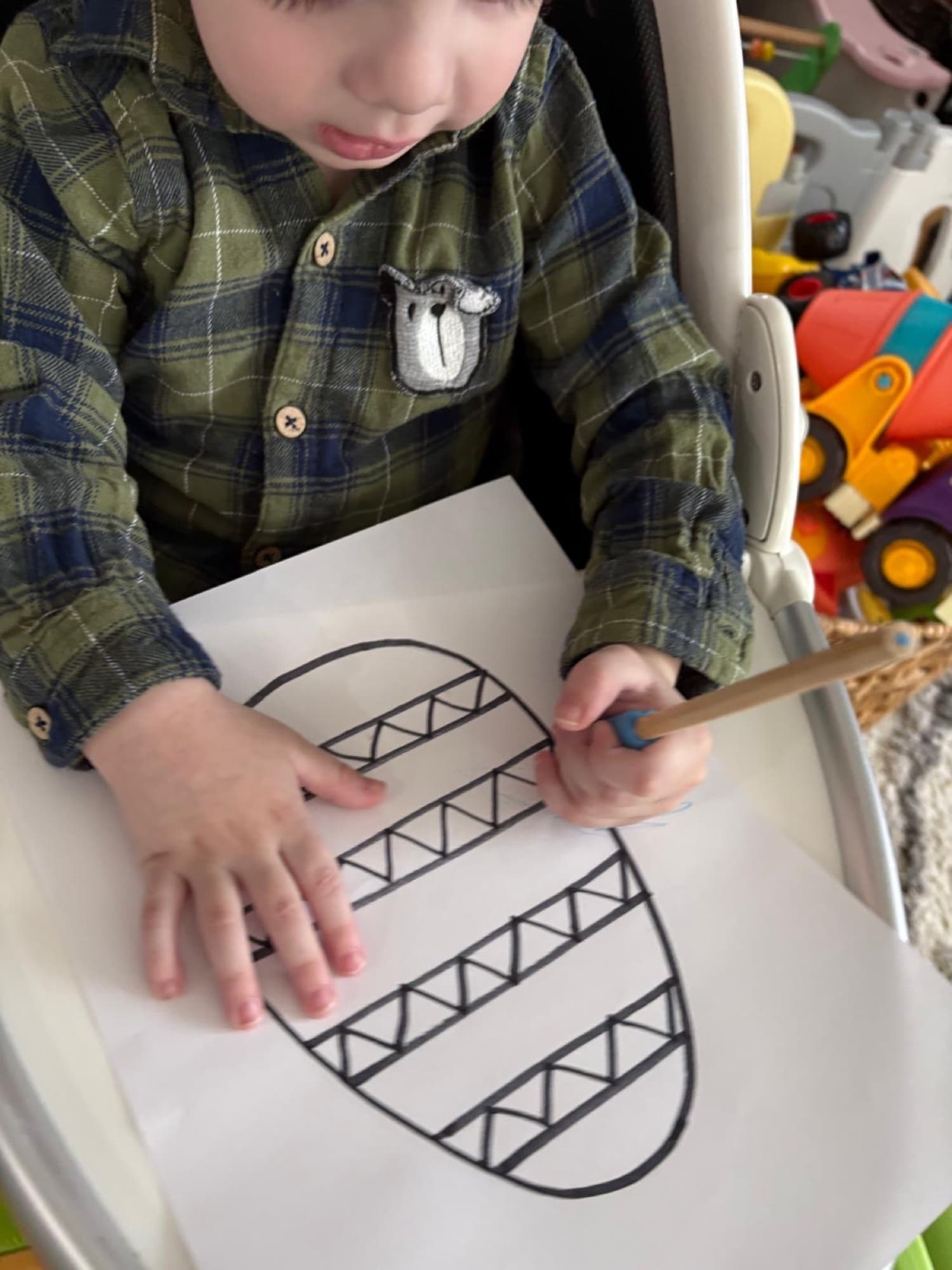 A toddler in a plaid shirt painting an Easter egg